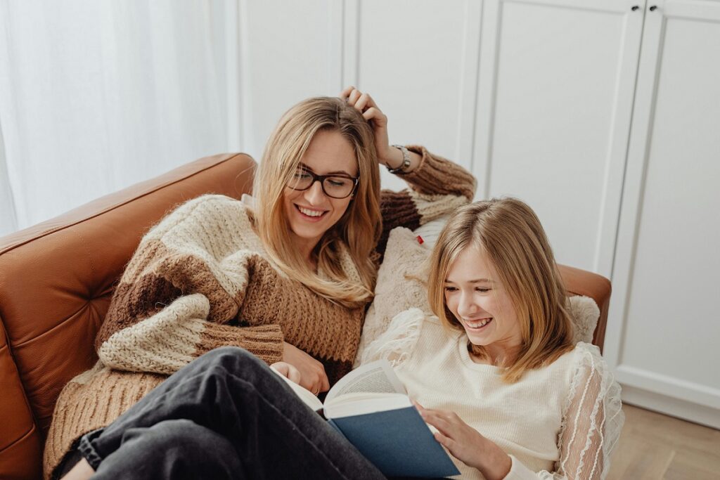 Ein Mutter liegt mit ihrer Tochter auf dem Sofa und liest mit ihr, beide lachen